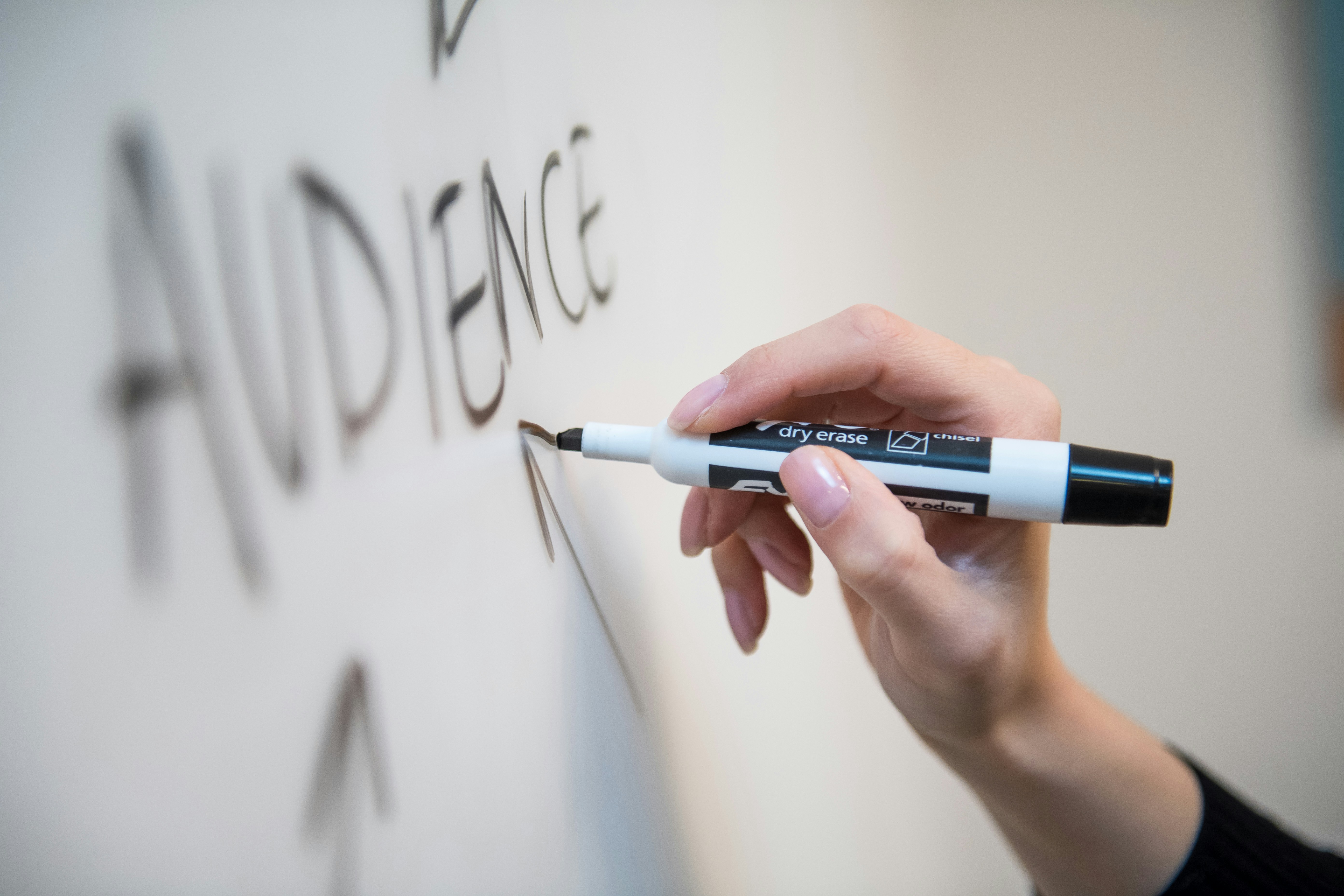 Woman's hand writing the word 'audience' on a whiteboard, with arrows.